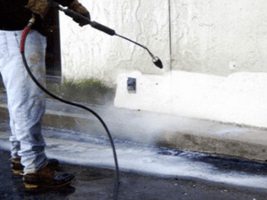 An Eight Five O employee pressure washing the side of a building. The cleaned area is bright white while the area yet to be cleaned is still dark gray.